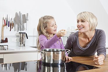 Germany, Bavaria, Munich, Daughter feeding mother in kitchen, smiling - RBYF000304