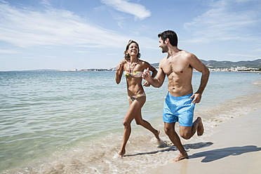 Spanien, Mid adult couple running on beach - WESTF018997