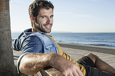 Spain, Mid adult man sitting on bench, smiling, portrait - WESTF019020