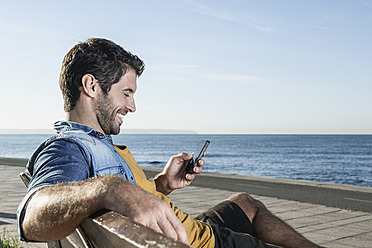 Spanien, mittelgroßer erwachsener Mann mit Smartphone, lächelnd - WESTF019021