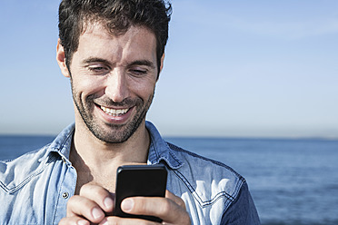 Spain, Mid adult man using smart phone, smiling - WESTF019024