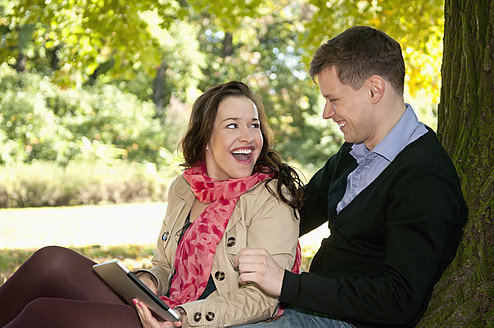 Deutschland, Berlin, Paar sitzt im Herbst Park mit digitalem Tablet, lächelnd - BFRF000120