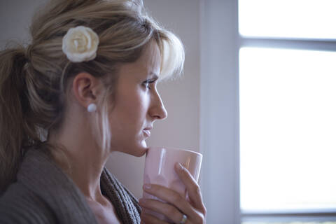 Junge Frau steht mit Kaffee am Fenster, lizenzfreies Stockfoto