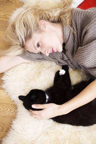 Junge Frau mit Katze auf Teppich liegend, lizenzfreies Stockfoto