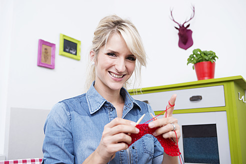 Young woman knitting with red yarn, smiling, portrait - VRF000098