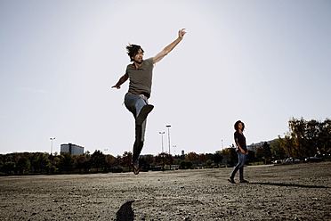 Germany, Cologne, Man jumping in field, woman standing in background - FMKF000495