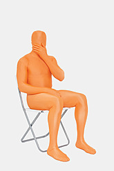 Älterer Mann in orangefarbenem Zentai mit Hand über dem Mund - TCF003045