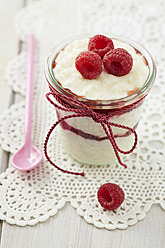 Milk rice pudding with raspberries and jam in glass on table - ECF000153