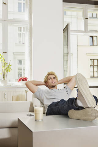 Deutschland, Berlin, Junger Mann sitzt im Wohnzimmer, lächelnd, lizenzfreies Stockfoto