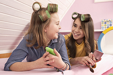 Girls with hair rollers lying and watching smartphone, smiling - RNF001078