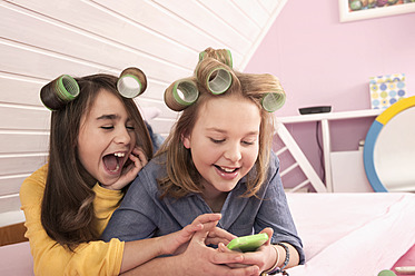 Girls with hair rollers lying and watching smartphone, smiling - RNF001079