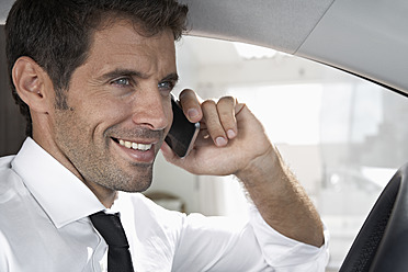 Spain, Businessman sitting in car and talking on mobile phone, smiling - PDYF000357