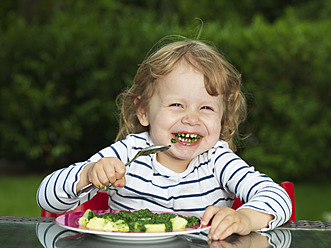 Germany, Duesseldorf, Girl sitting outside and eating spinach, smiling, portrait - STKF000044