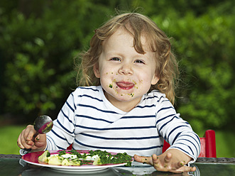 Germany, Duesseldorf, Girl sitting outside and eating spinach, smiling, portrait - STKF000046