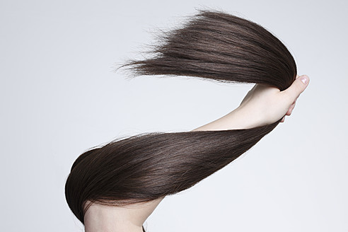 Human hand holding brown hair against white background, close up - STKF000072