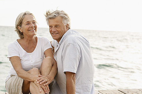 Spain, Senior couple sitting at the sea, smiling - JKF000014