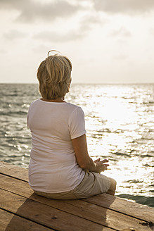 Spain, Senior woman sitting on jetty at the sea - JKF000033