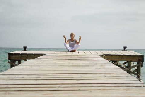 Spanien, Ältere Frau beim Yoga auf dem Steg am Meer, lizenzfreies Stockfoto