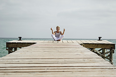 Spain, Senior woman doing yoga on jetty at the sea - JKF000041