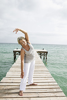 Spain, Senior woman doing yoga on jetty at the sea - JKF000044