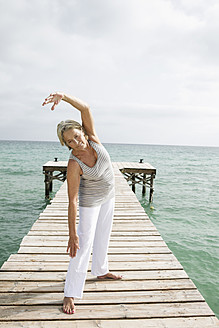 Spanien, Ältere Frau beim Yoga auf dem Steg am Meer - JKF000044