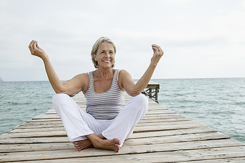 Spain, Senior woman doing yoga on jetty at the sea - JKF000045