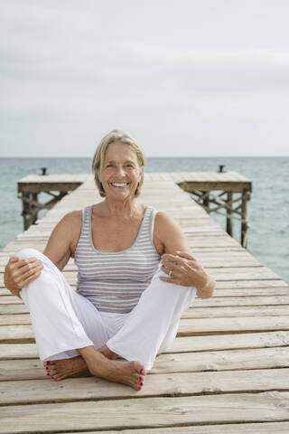 Spanien, Ältere Frau sitzt auf Steg am Meer, lizenzfreies Stockfoto