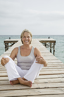 Spain, Senior woman sitting on jetty at the sea - JKF000046