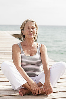 Spain, Senior woman doing yoga on jetty at the sea - JKF000048