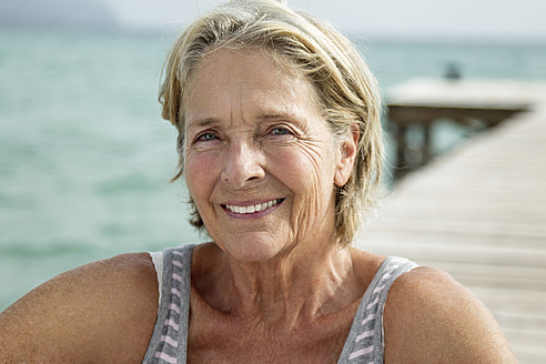 Spanien, Ältere Frau auf Steg am Meer sitzend, lächelnd, Porträt - JKF000050