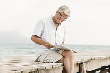 Spanien, älterer Mann liest Zeitung auf einem Steg am Meer - JKF000053