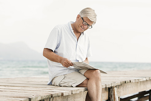 Spain, Senior man reading newspaper on jetty at the sea - JKF000053