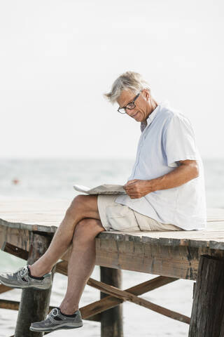 Spain, Senior man reading newspaper on jetty at the sea stock photo