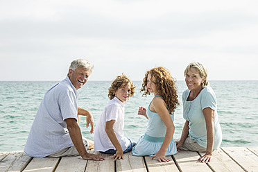 Spain, Grandparents with grandchildren sitting on jetty, smiling, portrait - JKF000066