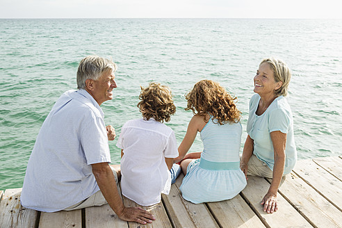 Spain, Grandparents with grandchildren sitting on jetty - JKF000069