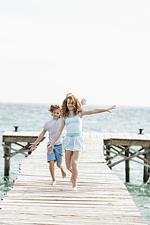 Spanien, Mädchen und Junge laufen auf Steg am Meer - JKF000072