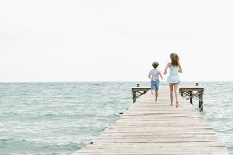 Spain, Girl and boy running on jetty at the sea stock photo