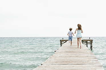 Spanien, Mädchen und Junge laufen auf Steg am Meer - JKF000073