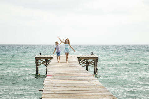 Spain, Girl and boy running on jetty at the sea stock photo