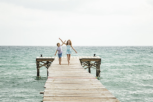 Spain, Girl and boy running on jetty at the sea - JKF000074