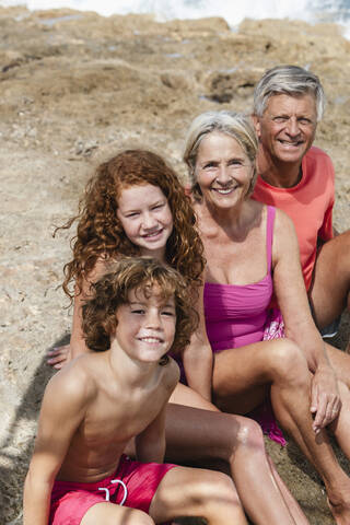 Spanien, Großeltern mit Enkelkindern am Strand sitzend, lächelnd, Porträt, lizenzfreies Stockfoto