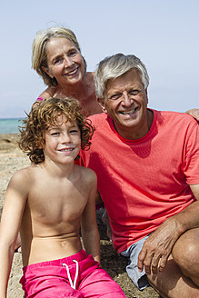 Spanien, Großeltern mit Enkel am Strand sitzend, lächelnd - JKF000094