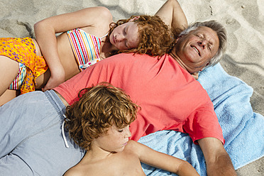 Spain, Grandfather and grandchildren relaxing on beach - JKF000096