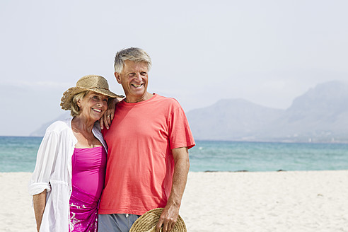 Spanien, Seniorpaar am Strand stehend, lächelnd - JKF000112