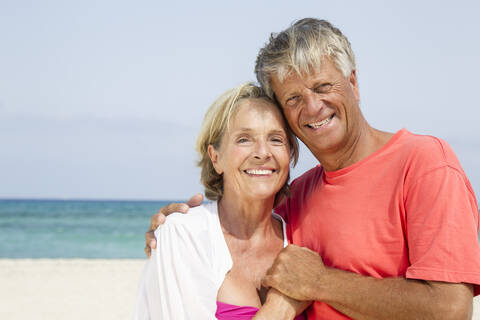 Spanien, Seniorpaar am Strand stehend, lächelnd, Porträt, lizenzfreies Stockfoto