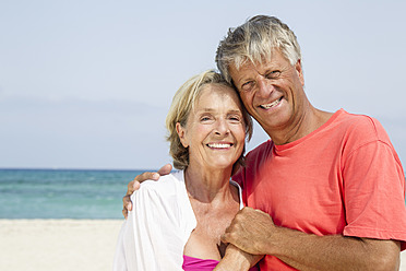 Spanien, Seniorpaar am Strand stehend, lächelnd, Porträt - JKF000113