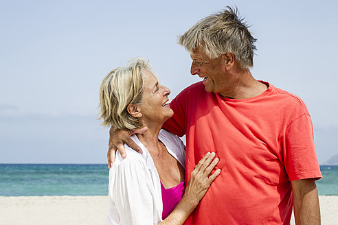 Spain, Senior couple romancing at beach, smiling - JKF000114