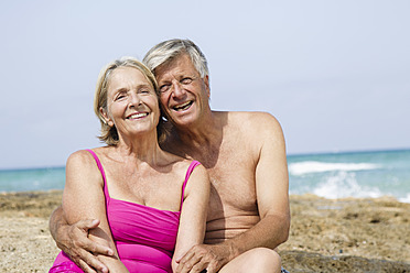 Spain, Senior couple sitting on rock at beach, smiling - JKF000118