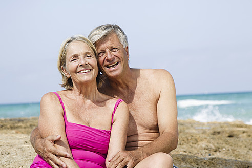 Spanien, Älteres Paar sitzt auf einem Felsen am Strand, lächelnd - JKF000118
