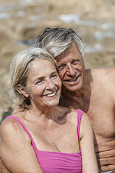 Spain, Senior couple sitting on rock at beach, smiling - JKF000122